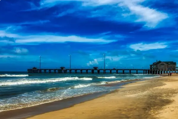 Outer Banks beach with soft dunes, sea grass, and a historic lighthouse in the distance.